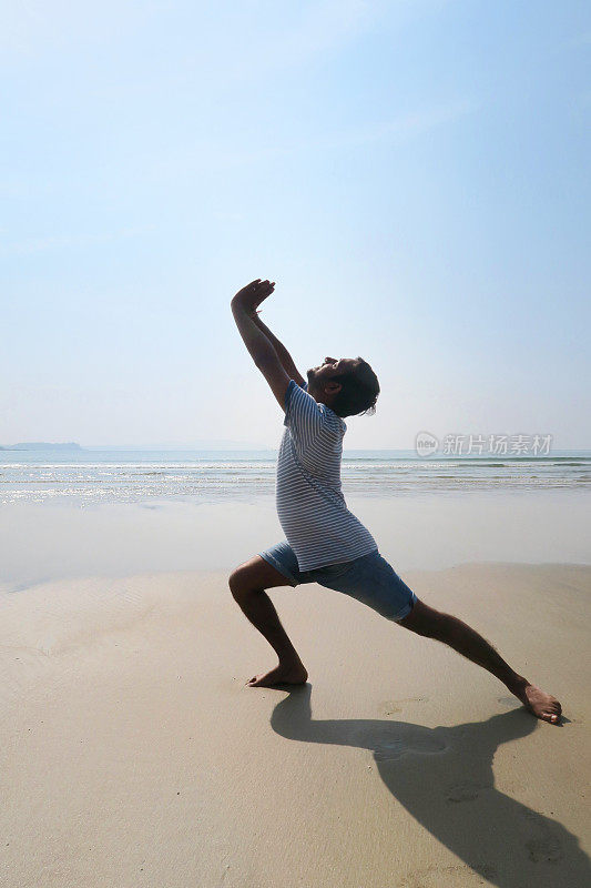 印度人练习武士I姿势(Virabhadrasana I)瑜伽姿势在潮湿的沙滩上，水的边缘，Palolem海滩，果阿，印度